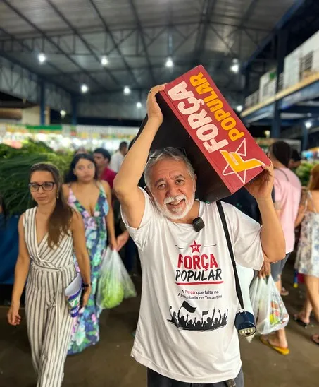 Freitas do PT carrega uma placa da Força Popular no ombro numa feira
